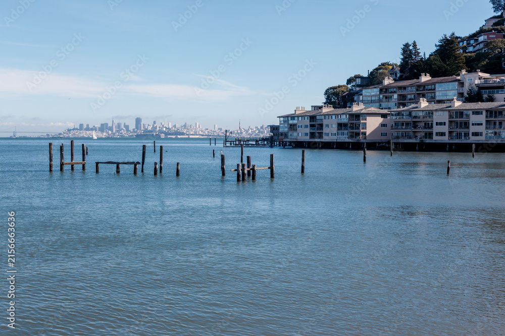 Fototapeta premium The San Francisco skyline seen across the bay from the wooden pilings of waterfront homes in Sausalito, California, USA.