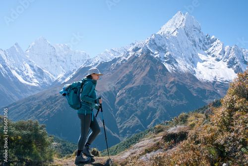 Female hiker with backpack and trekking poles walking on mountain trail with majestic Mount Ama Dablam in background, Nepal Himalayas.