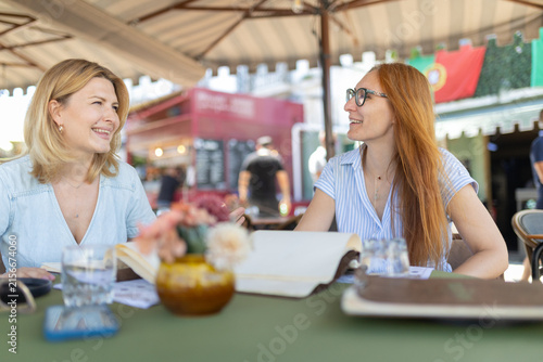 Fotografía Women talk and enjoy drinks at a cafe in a busy outdoor setting on a sunny day i