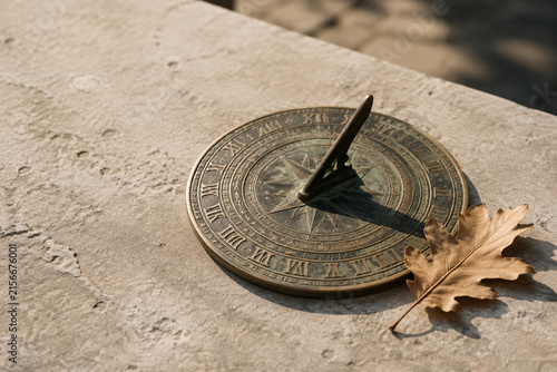 Antique bronze sundial with dried oak leaf on grey stone, time and history concept