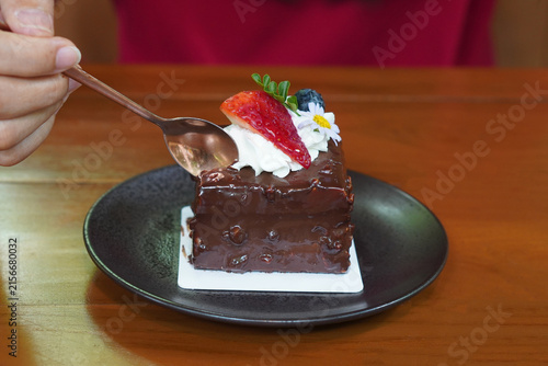 Use a brass spoon to scoop the chocolate cake decorated with a strawberry, a blueberry, and flowers and leaves, brass spoon and fork, placed on a sheet of paper top a black ceramic plate.jpg