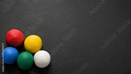 Five colorful modeling clay balls on a dark textured background with copy space