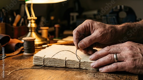 Closeup of hands binding a handmade book with thread and needle in a warm wood workshop