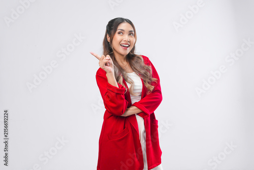 Smiling young Asian woman wearing red jacket is pointing to the copy space behind her.