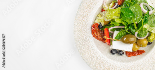 Fresh Mediterranean salad with mixed greens, olives, sun-dried tomatoes, and feta cheese served in a textured white bowl against a clean, light background