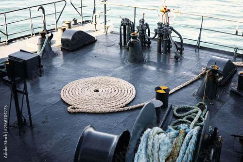 Bild auf Leinwand Coiled mooring rope neatly arranged on a steel ship deck beside winches and bollards, nautical equipment bathed in soft light with calm sea visible beyond; industrial, maritime and travel atmosphere