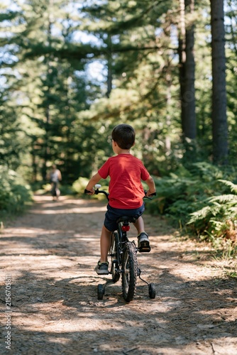 Child on small bicycle with training wheels riding along forest path for outdoor activity background and banner design with nature scenery