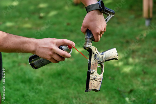 Fotografía Close-up of hands spraying lubricant into a AR rifle lower while performing outdoor maintenance on grass