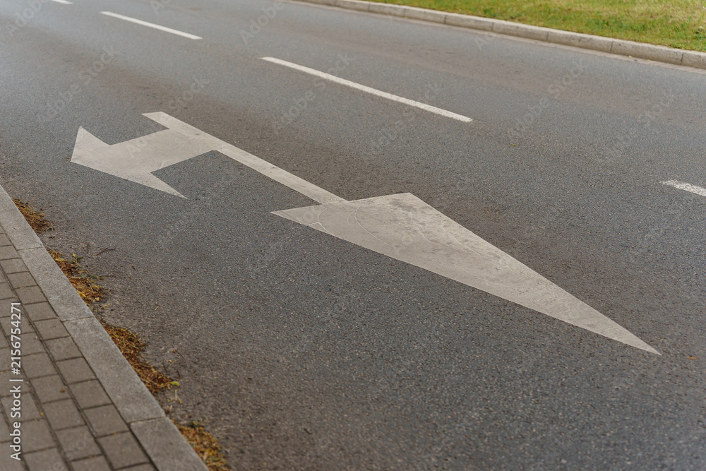 Obraz premium White painted arrow on asphalt road surface showing left and straight traffic direction, typical urban transportation infrastructure element