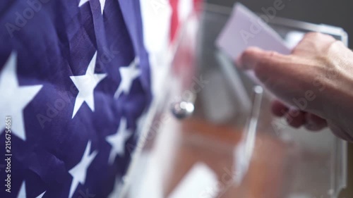 High angle of voter dropping ballot into transparent box with US flag on background