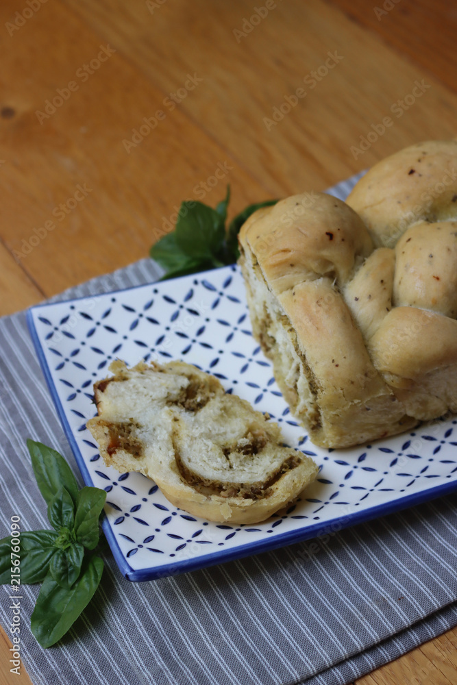 Fototapeta premium Braided bread with green basil pesto sauce on a decorated ceramic tray on wooden table with copy space