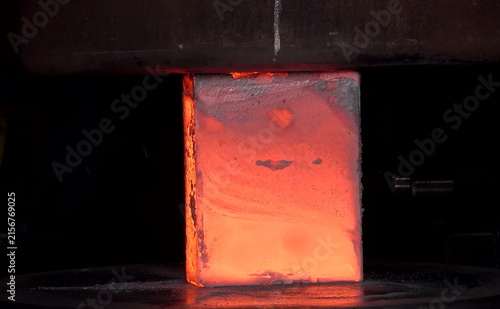 Obraz na płótnie A heated cylindrical metal block glows bright orange as sparks and fragments scatter under compression, showing the intensity and precision of industrial forging at extreme temperature levels