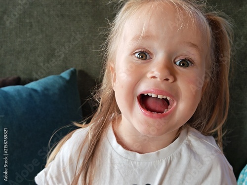 Obraz na plátně Close-up portrait of a joyful little girl laughing at home, cheerful childhood emotion, playful expression, family lifestyle, and candid photography