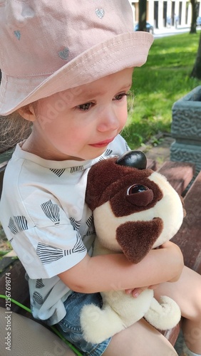 Fotografie Upset little girl with tears in her eyes holding a plush dog outdoors, childhood sadness, comfort toy, emotional support, and tender portrait