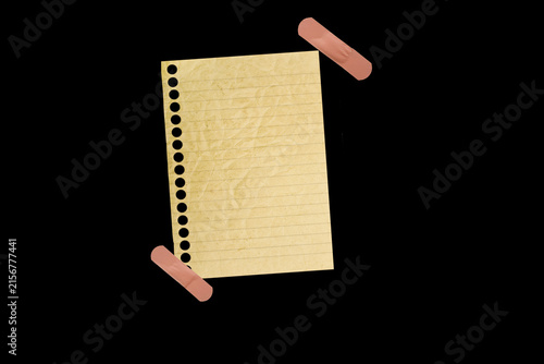 Foto Piece of notebook paper patched with a torn bandage, isolated black JPEG