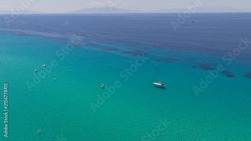 Turquoise Greek sea showing an anchored sailboat scattered