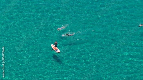 Paddleboarder and swimmers enjoying crystal clear turquoise sea