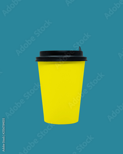 Yellow disposable coffee cup with black lid isolated on teal background. Blank mockup and template for creative design, branding and packaging projects. Minimalist product photography concept.