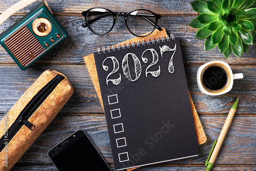 New year resolutions 2027 on desk. 2027 goals list with notebook, coffee cup, plant on wooden table. Resolutions, plan, goals, action, checklist, idea concept. New Year 2027 resolutions. Copy space