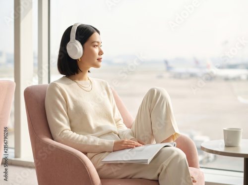 Young woman with noise-cancelling headphones relaxing in an airport lounge, representing premium travel comfort and elegant lifestyle