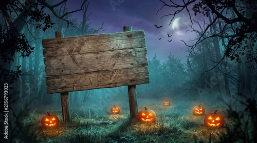 Spooky halloween background with empty wooden sign and glowing pumpkins in a misty forest