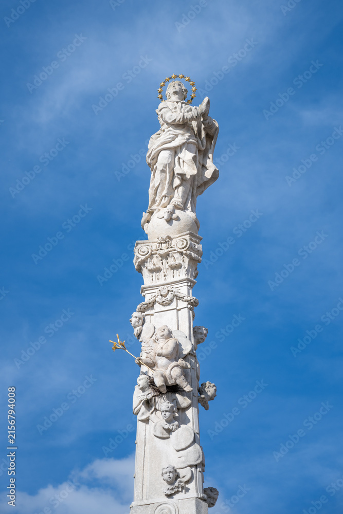 Fototapeta premium The Marian Column is located in Masaryk Square in Trebon. It features a statue of the Virgin Mary and angels. The setting has clear blue skies and is a notable landmark.
