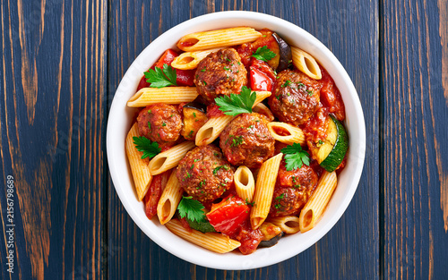 Penne pasta with meatballs in tomato sauce and vegetables in bowl. Top view. Flat lay