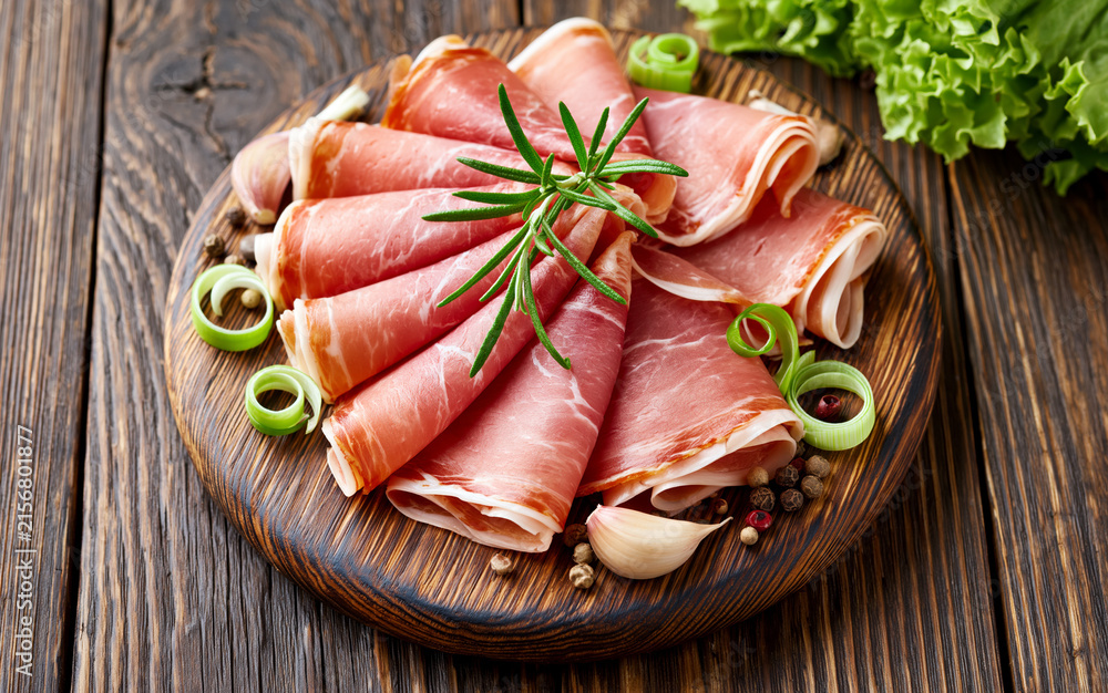 Fototapeta premium Slices of Prosciutto on old wooden background. Top view