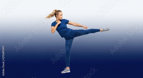 Athletic Woman in Blue Workout Outfit Performing High Kick in Gradient Blue Background