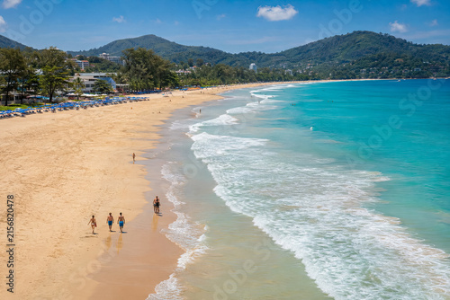 High angle view of a broad Phuket beach with rolling white waves and tiny walkers on the sand.generative AI
