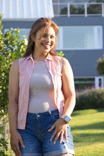 African American woman standing near shrubs in front yard of house wearing denim shorts, smartwatch