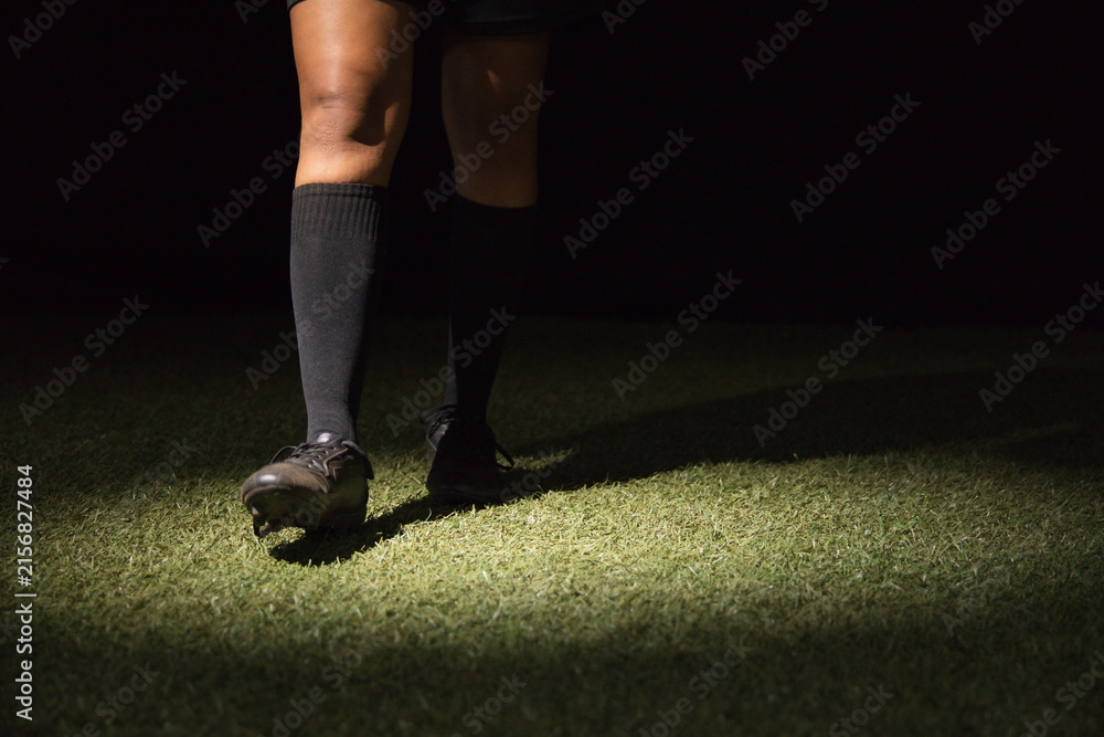 Fototapeta premium Female soccer player standing on turf at night wearing knee-high socks and cleats under spotlight