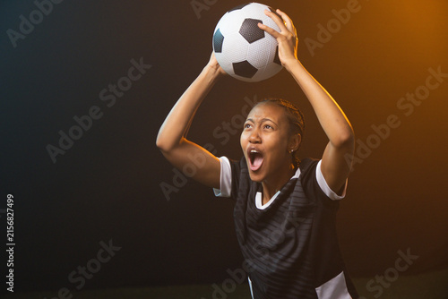 Adult African woman holding BW ball overhead shouting in BW-jersey braids ring warm-rim, copy space