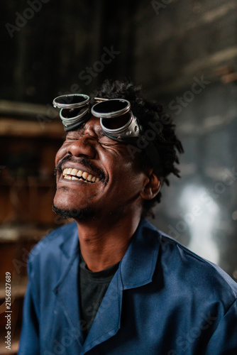 Man wearing welding goggles smiles in workshop