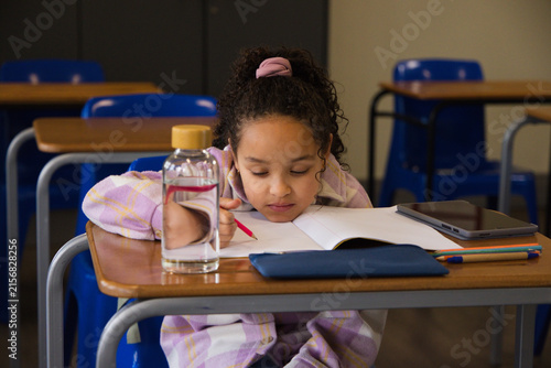 African American child sitting at school desk writing notebook holding pink pencil in pink plaid