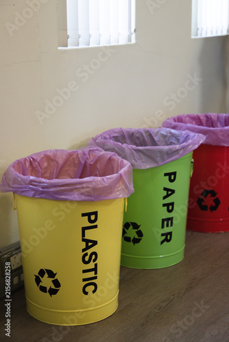 Yellow metal recycling bin is sitting with green and red bins against pale wall, purple liners