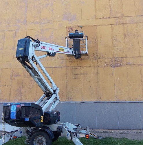 Trailer-Mounted Articulated Boom Lift Reaching Yellow Building Facade for Maintenance.

