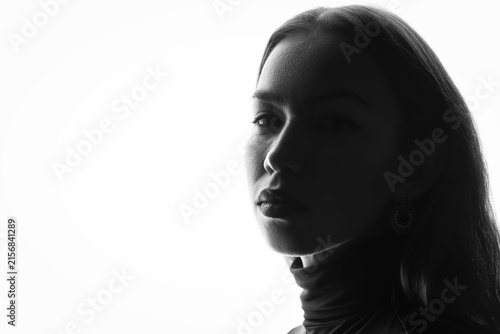 Konstfotografi Backlit side profile of a young caucasian woman with a hoop earring against a bright high key background, a deep shadow across her face and a large empty area for text