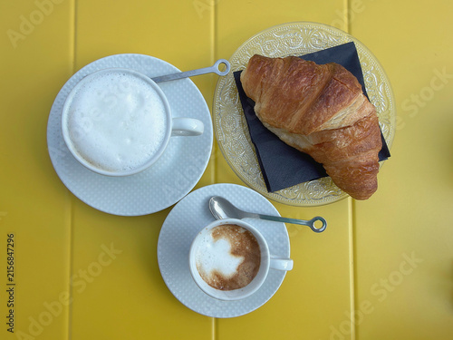 croissant and cup of coffee on yellow table