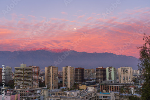 The urban skyline of Santiago city with high-rise apartment buildings under a vibrant pink sunset sky near the Andes mountains in Chile