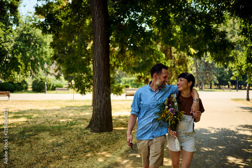 Fotografie Couple Walking in Park With Wildflower Bouquet Sharing a Warm Moment on a Summer