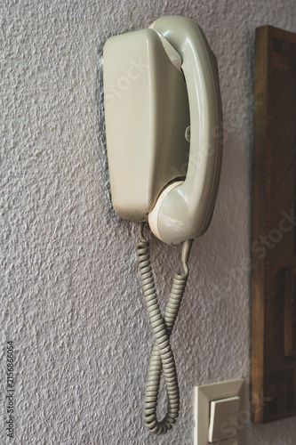 Vintage beige wall-mounted intercom telephone handset on a textured plaster wall in an apartment entry.