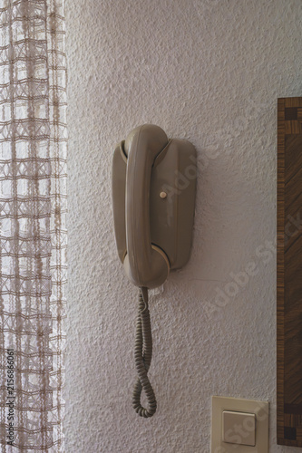 Vintage beige wall-mounted intercom telephone handset on a textured plaster wall in an apartment entry.