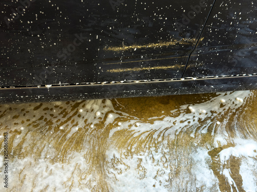 Soapy water and foam dripping from a dark car door onto the wet concrete floor at a car wash.