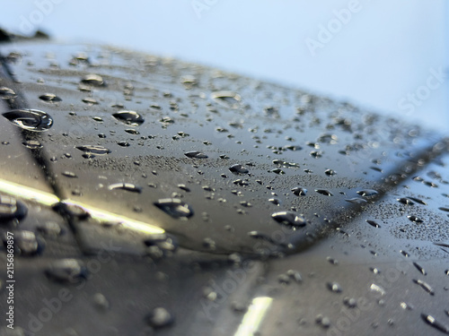 Macro close-up of water droplets and beads on a glossy black car hood showing hydrophobic coating.