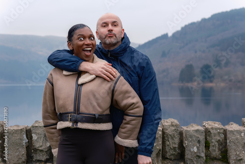 Funny Interracial Couple Making Silly Faces by Misty Lake with Playful Hug
