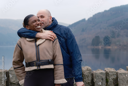 Laughing Interracial Couple Embracing by Misty Lake as Man Kisses Woman on Cheek