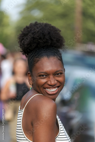 Joyful Young Black Woman with Natural Afro Puff Laughing Over Shoulder on Summer Street