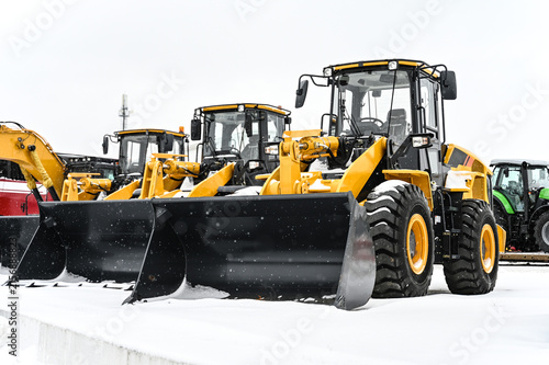 Front-end loaders and other construction machinery parked at an equipment yard. Heavy equipment ready for use in construction, earthmoving, roadwork, and infrastructure projects.