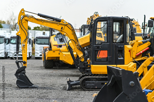 Mini excavator and other construction machinery parked in an equipment yard. Heavy equipment ready for work, transport, or use at construction and infrastructure sites.